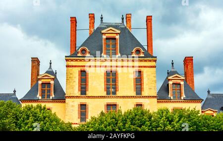 Frontal view of the Cour des Offices building, part of the Chateau de Fontainebleau (Palace of Fontainebleau), under a cloudy sky. Seine-et-Marne, Fra Stock Photo