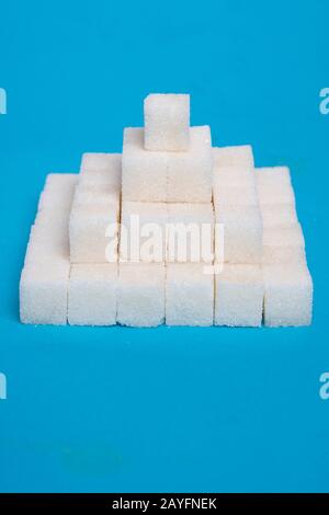 Sugar cubes pyramid on a blue paper, creative food idea, vertical Stock Photo