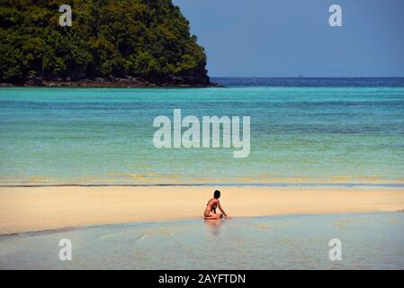 woman in bikini sitting on sandy beach, Thailand, Koh Phi Phi Stock Photo
