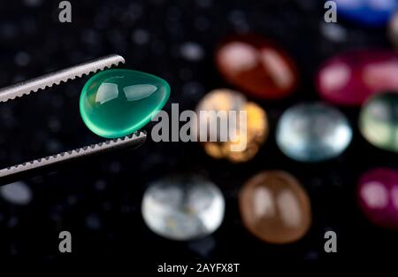 Round cut emerald mineral gemstone with dark stones background. Stock Photo