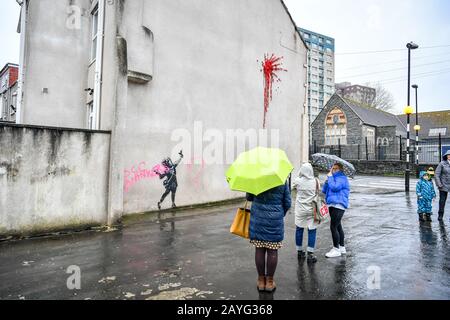 NOTE IMAGE CONTAINS SWEAR WORD People photograph a Banksy work of art on the side of a house on Marsh Lane, Barton Hill, Bristol, which has been vandalised with pink spray paint, the day after it was confirmed on Valentine's Day. Stock Photo