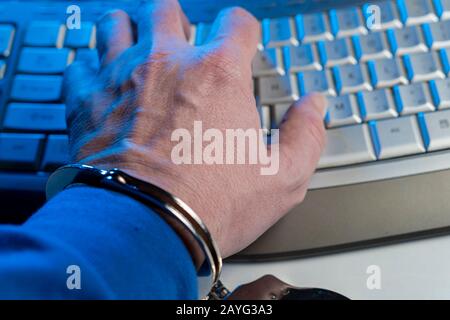 Hand of a man in handcuffs on a background of a computer keyboard Stock Photo