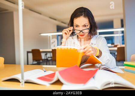 Surprised Woman reading Book in library Stock Photo