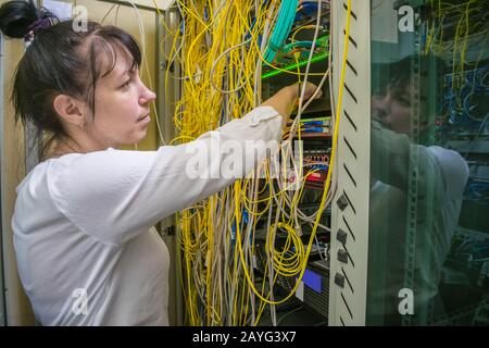 The woman switches the fiber wires in the server room. A specialist commutes an optical Internet cable in a rack with powerful computer equipment. Gir Stock Photo