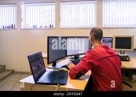 The engineer monitors the computer network. The system administrator looks at multiple monitors. A man is sitting at the office behind a worker's desk Stock Photo