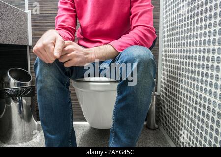 A man in jeans is sitting on the toilet in a public toilet Stock Photo