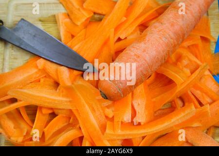 Close up of isolated raw fresh carrot cut in stripes with blade of japanese kitchen knife on wood cutting board Stock Photo