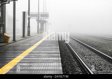 Empty train station platform in the morning of foggy day - monochrome image with yellow colour Stock Photo