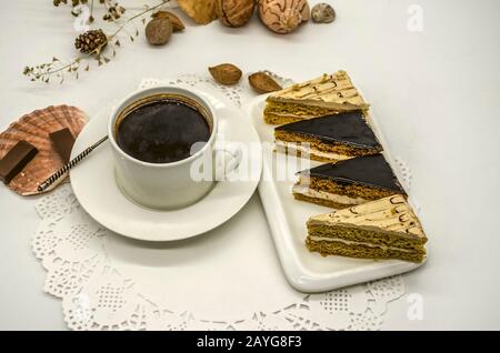 Slices of cream cakes on a platter, black coffee in a white cup with a silver spoon among seashells and dried twigs on a white paper napkin Stock Photo