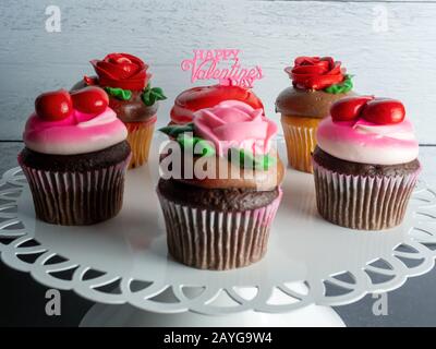 White metal platter filled with cupcakes decorated for Valentine’s Day with a pink sign and pink and red roses and hearts, perfect for love. Stock Photo