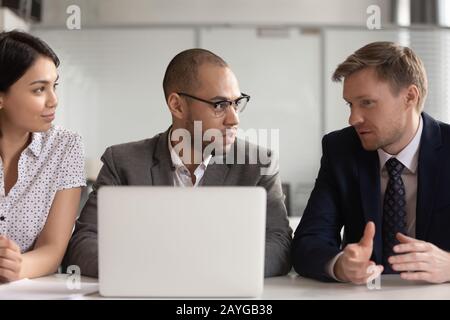 Diverse employees work at laptop discussing project together Stock Photo