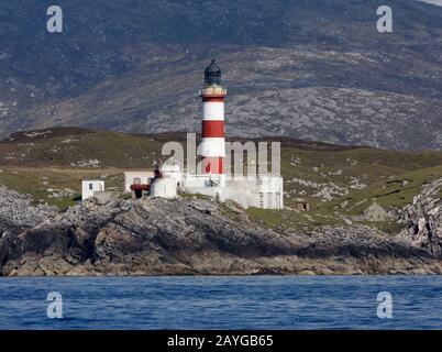 The tall, red and white striped Eilean Glas lighthouse, Scalpay, from the sea, with the hills of Harris behind, Western Isles, Scotland Stock Photo