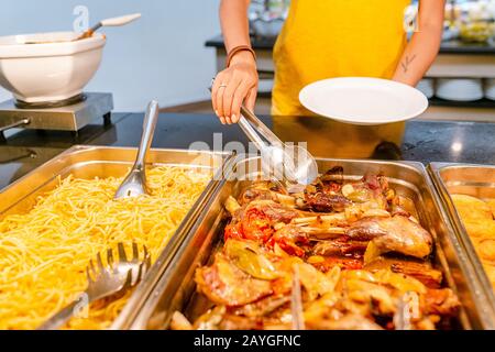 Woman choosing and picking various snacks and dishes on a table at the buffet in hotel restaurant. All you can eat Stock Photo