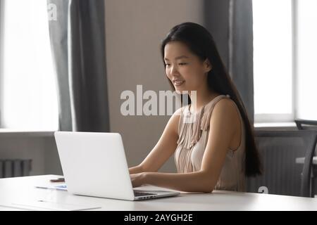 Millennial Asian woman busy working on laptop in office Stock Photo