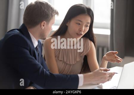 Multiethnic employees discuss project working on laptop in office Stock Photo
