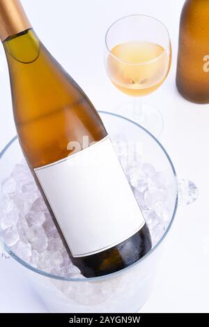 Closeup of a White Wine bottle with blank label in an crystal ice bucket with a glass and bottle in the background . Stock Photo