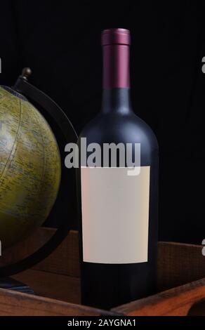 Closeup of a red wine bottle with a blank label in a wood crate with antique world globe. Stock Photo