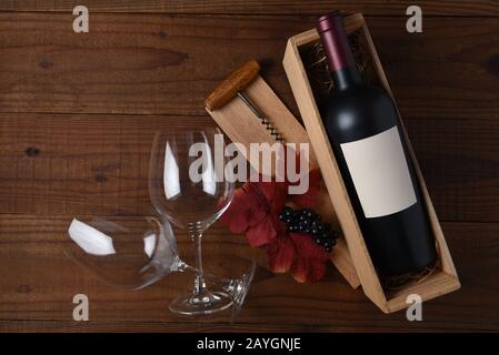 Wine Still Life  A bottle of wine with blank label in a wood box with two glasses, corkscrew, leaves and grapes. Flat Lay with copy space on rustic da Stock Photo