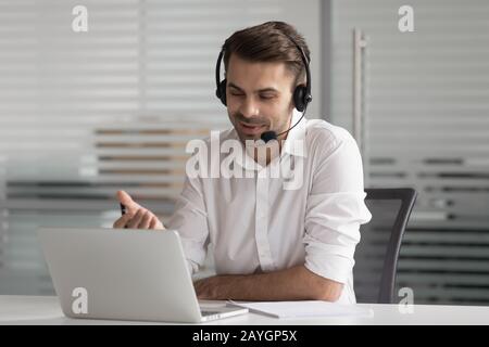Smiling male worker in headset talking on video call Stock Photo
