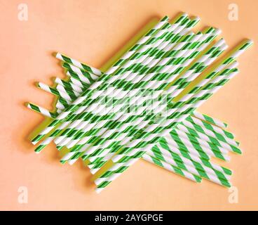 Top view of colorful paper disposable eco-friendly straws. Drinking straws with green strips for party on orange background with copy space. Eco waste Stock Photo