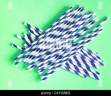 Top view of colorful paper disposable eco-friendly straws. Drinking straws with blue strips for party on green background with copy space. Eco waste c Stock Photo