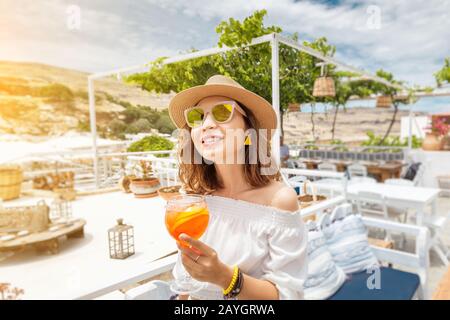 Happy asian woman enjoying aperol spritz cocktail in a greek cafe. Beverage and refreshment concept Stock Photo