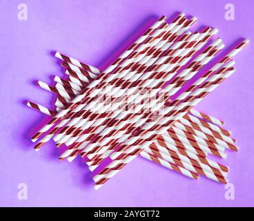 Top view of colorful paper disposable eco-friendly straws. Drinking straws with red strips for party on purple background with copy space. Eco waste c Stock Photo