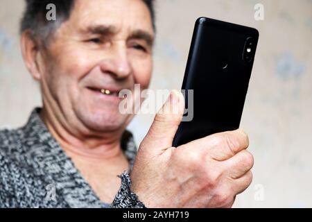 Happy elderly man using smartphone, mobile phone in male hands close up, selective focus. Concept of online communication for retired, watching video Stock Photo