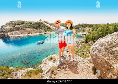 A couple in love hugs and holds a Greek flag, posing against the blue Paradise lagoon. Travel to Greece Stock Photo