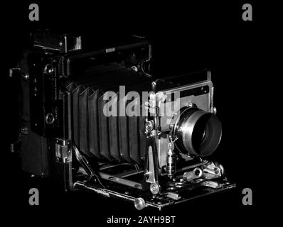 Vintage Speed Graphic medium format film camera on a black background. Side view, low key lighting, black and white photo. Stock Photo