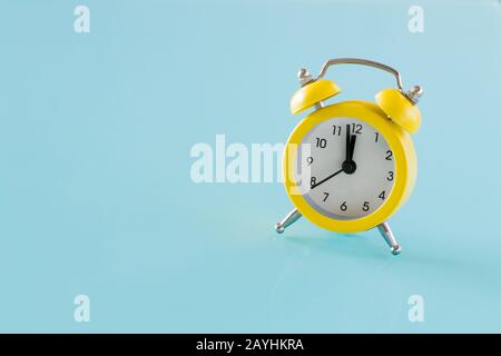 A small yellow alarm clock on a blue glass. Place for text Stock Photo
