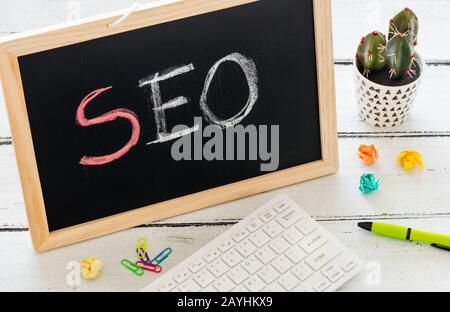 SEO inscription in chalk on the school board, Search engine optimization and websites. Desk, swept balls of paper, computer keyboard Stock Photo