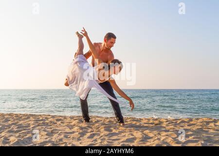 Athletic fit young couple at the beach practicing acro yoga fitness workout exercises, balancing in pair on a summer day at dusk. Healthy lifestyle an Stock Photo