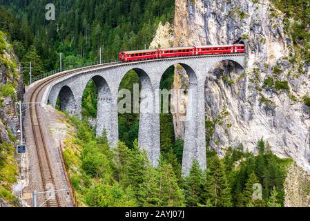 Landwasser Viaduct in Filisur, Switzerland. It is a famous landmark of Swiss Alps. Red express train on high bridge in mountains. Scenic view of amazi Stock Photo