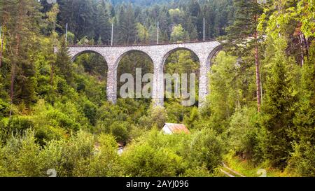 Landscape with high bridge and small house, Filisur, Switzerland. Panorama of Alpine forest. Scenic view of viaduct in summer. Mountain landscape with Stock Photo