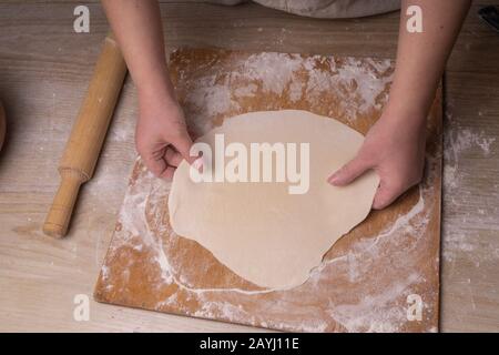 A woman rolls out the dough. Plywood cutting board, wooden flour sieve and wooden rolling pin - tools for making dough Stock Photo