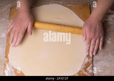 A woman rolls out the dough. Plywood cutting board, wooden flour sieve and wooden rolling pin - tools for making dough Stock Photo