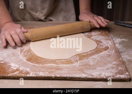 A woman rolls out the dough. Plywood cutting board, wooden flour sieve and wooden rolling pin - tools for making dough Stock Photo