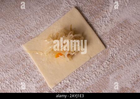 A rectangular piece of dough with cabbage - for making ravioli dumplings. Plywood cutting board, wooden flour sieve and wooden rolling pin - tools for Stock Photo