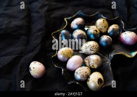 Colored chicken and quail eggs of pink, silver, golden and blue color on black Stock Photo