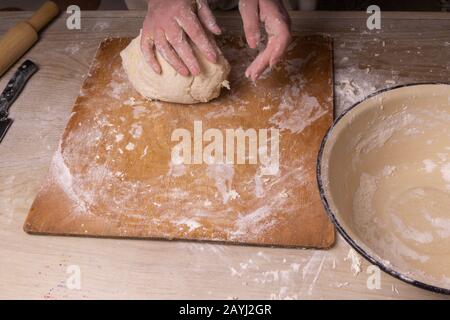 A woman kneads the dough. Plywood cutting board, wooden flour sieve and wooden rolling pin - tools for making dough Stock Photo