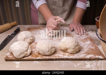 A woman kneads the dough. Plywood cutting board, wooden flour sieve and wooden rolling pin - tools for making dough Stock Photo