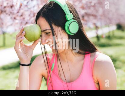 Portrait of happy smiling young beautiful woman in fitness wear with apple, outdoors Stock Photo
