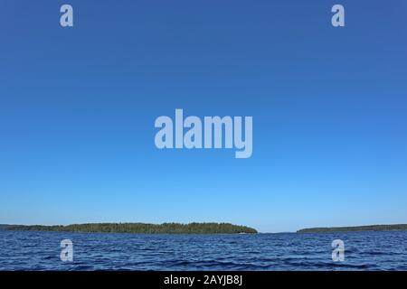 Blue water clear sky sunny day on finnish lake water waves close up. Beauty of nature skyline and forest with deep colored water. Photo from boat Stock Photo