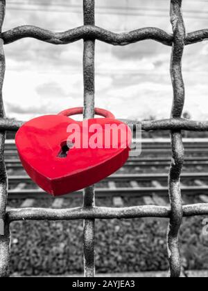 Red heart-shaped rusty padlock chained to a railing at the monochrome background. Stock Photo