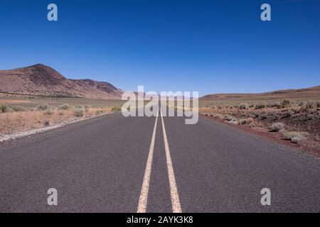 Straight asphalt road running between hills into the horizon. A road in a high desert of South Oregon Stock Photo