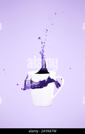 Levitating coffee mug with splashes. Coffee concept. Minimal art trend. Solid background. Vertical, straight cup, ultra violet tone, color of the year Stock Photo