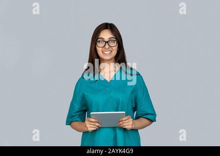 Happy young adult indian woman in doctor uniform holding tablet computer Stock Photo