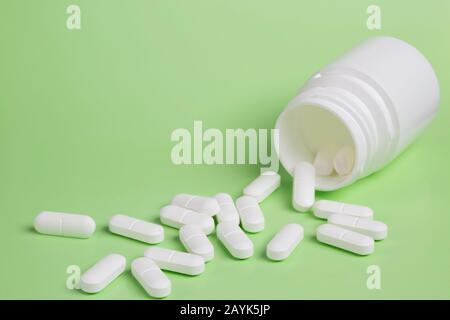 Plastic white bottles of pills on a green background of scattered white pills Stock Photo