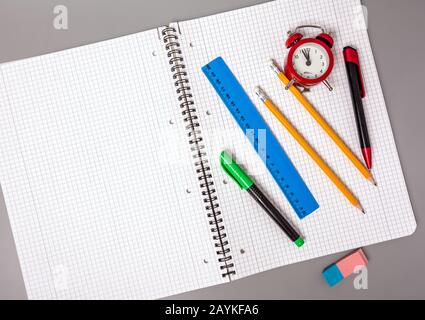 Pencils, a pen and a ruler lie on an open notebook. An alarm clock reminds of time. Office. School supplies.